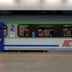 Pociąg PKP Intercity z dostępnym intercity wifi. Widać pasażerów w środku i mężczyznę stojącego na peronie.