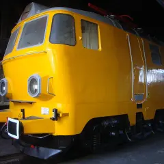 Żółta lokomotywa, model ep23, stoi w ciemni. Ma okrągłe reflektory i błyszczący lakier.