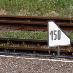 Biały trójkątny wskaźnik w11 z czarną liczbą 150 obok torów kolejowych.