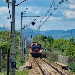 Pociąg PKP Łódź Kaliska - Krynica-Zdrój zbliża się do stacji, mijając zielone wzgórza i słupy trakcyjne.