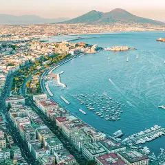 Widok na Neapol i Wezuwiusza. W oddali widać góry. W zatoce cumują łodzie. Można stąd ruszyć pociągiem do Sorrento.