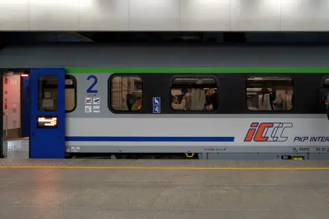 Pociąg PKP Intercity z dostępnym intercity wifi. Widać pasażerów w środku i mężczyznę stojącego na peronie.
