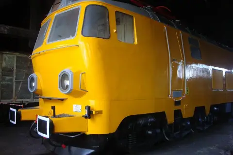 Żółta lokomotywa, model ep23, stoi w ciemni. Ma okrągłe reflektory i błyszczący lakier.