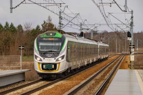 Nowoczesny pociąg 45WE-006E z zielonymi akcentami mija peron, gotowy do dalszej podróży.
