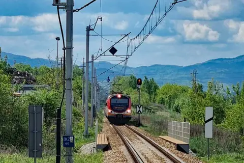 Pociąg PKP Łódź Kaliska - Krynica-Zdrój zbliża się do stacji, mijając zielone wzgórza i słupy trakcyjne.