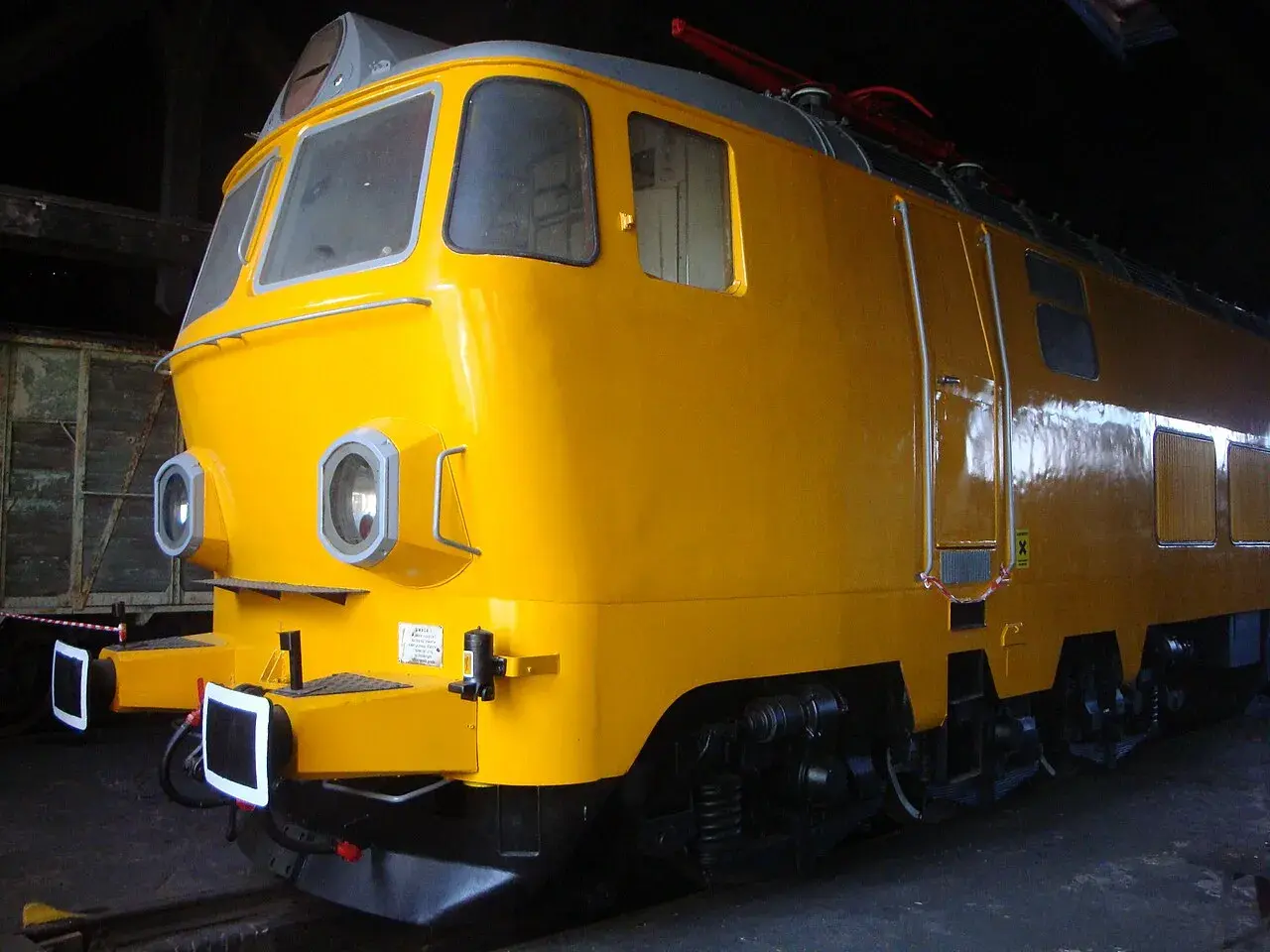 Żółta lokomotywa, model ep23, stoi w ciemni. Ma okrągłe reflektory i błyszczący lakier.