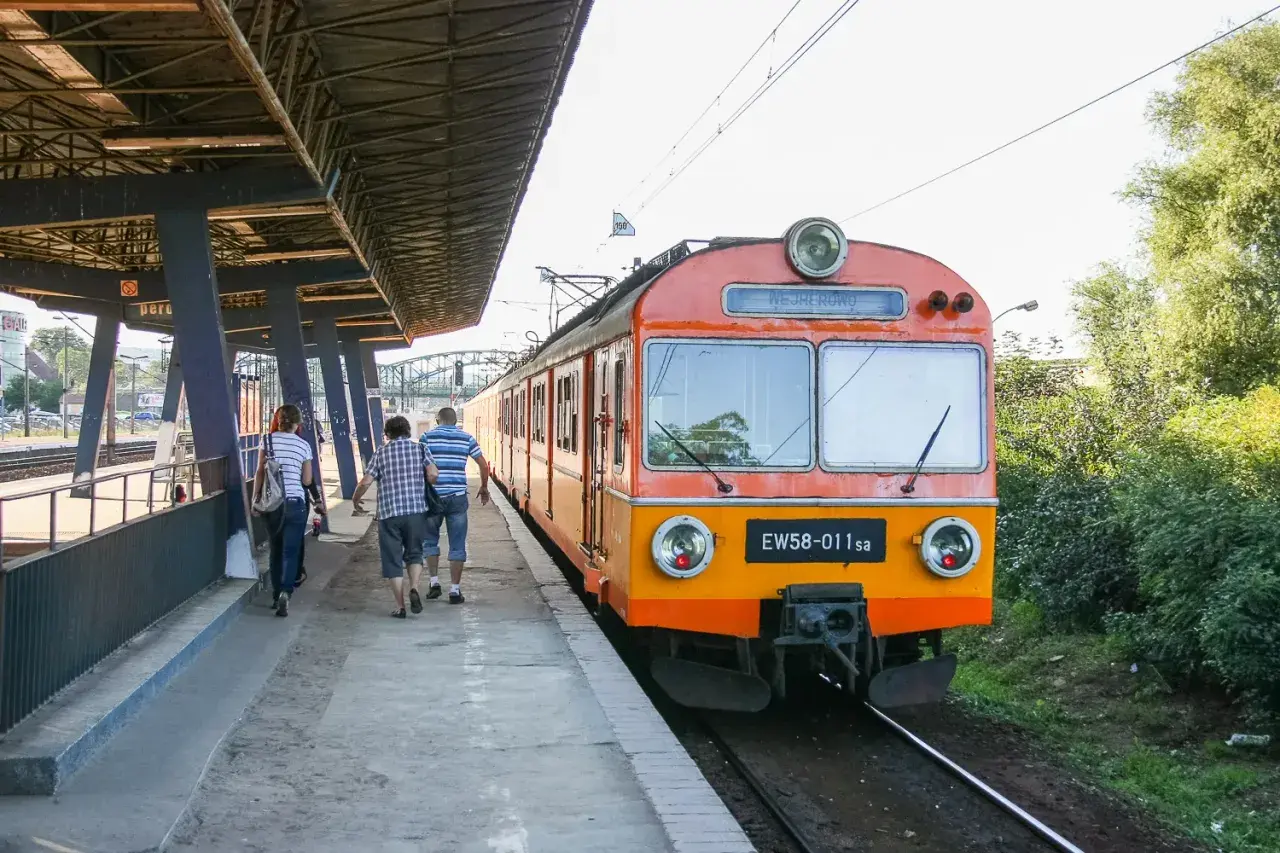 Pasażerowie idą wzdłuż peronu do pociągu EW58-011sa, który czeka na odjazd.