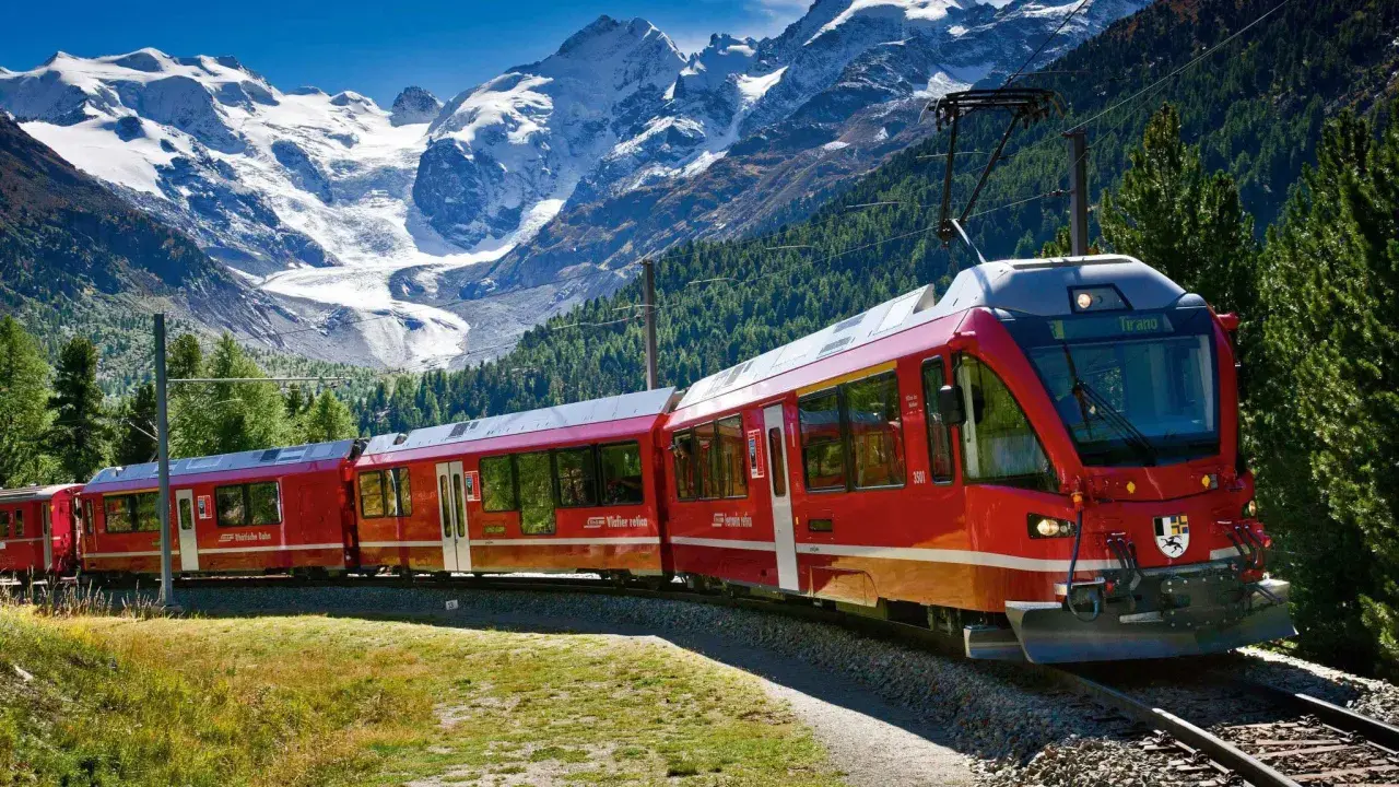 Czerwony pociąg Bernina Express na malowniczej trasie wśród alpejskich szczytów i zielonych lasów.