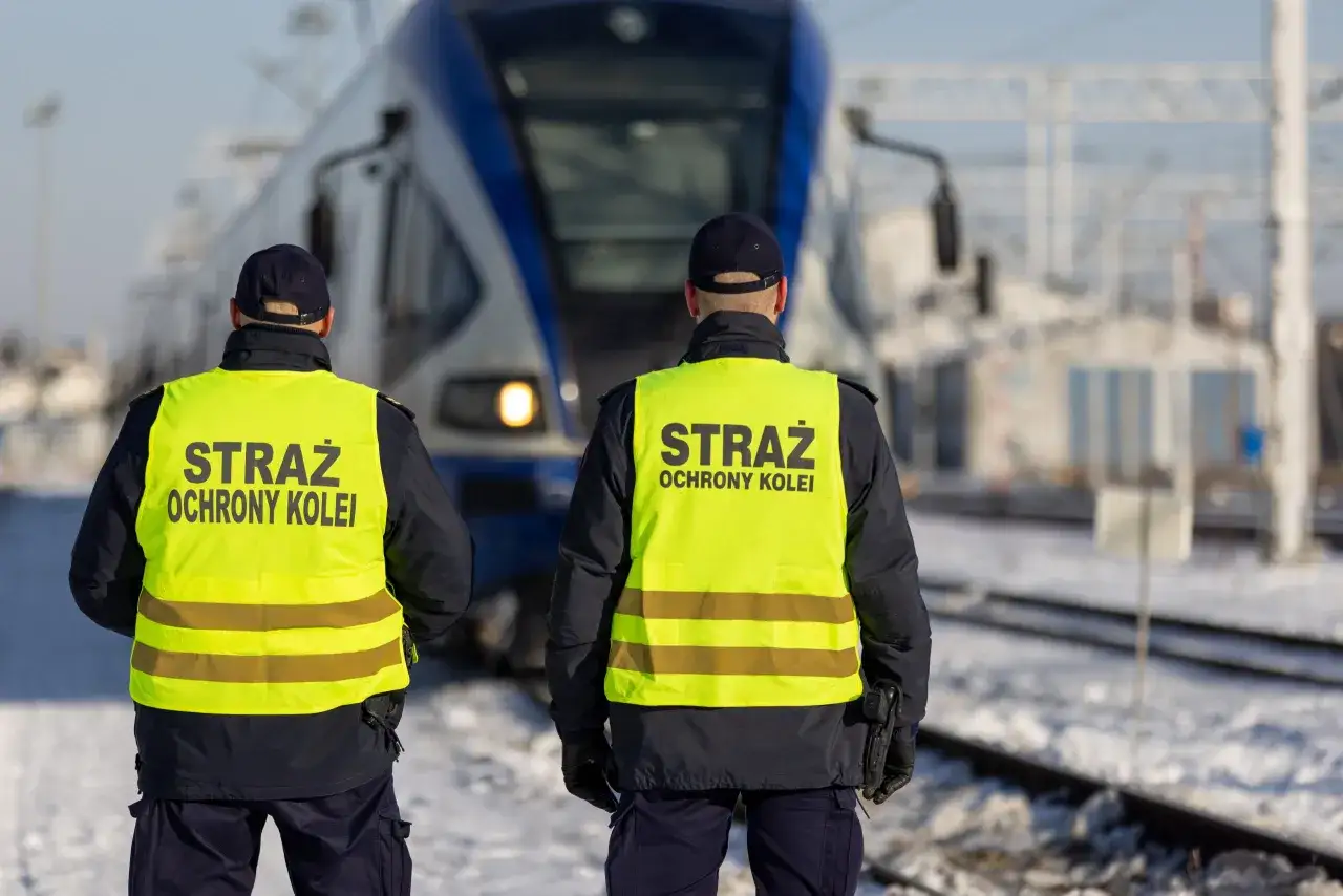 Dwóch funkcjonariuszy Straży Ochrony Kolei w kamizelkach odblaskowych stoi przed pociągiem. Czy mogą wystawić mandat?