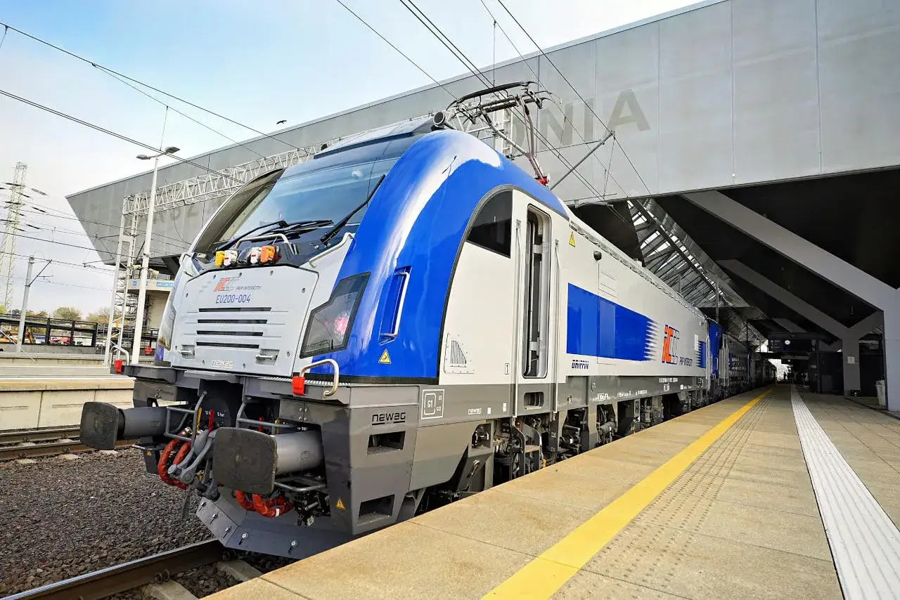 Nowoczesna lokomotywa EU200-004 PKP Intercity w biało-niebieskich barwach stoi na peronie.