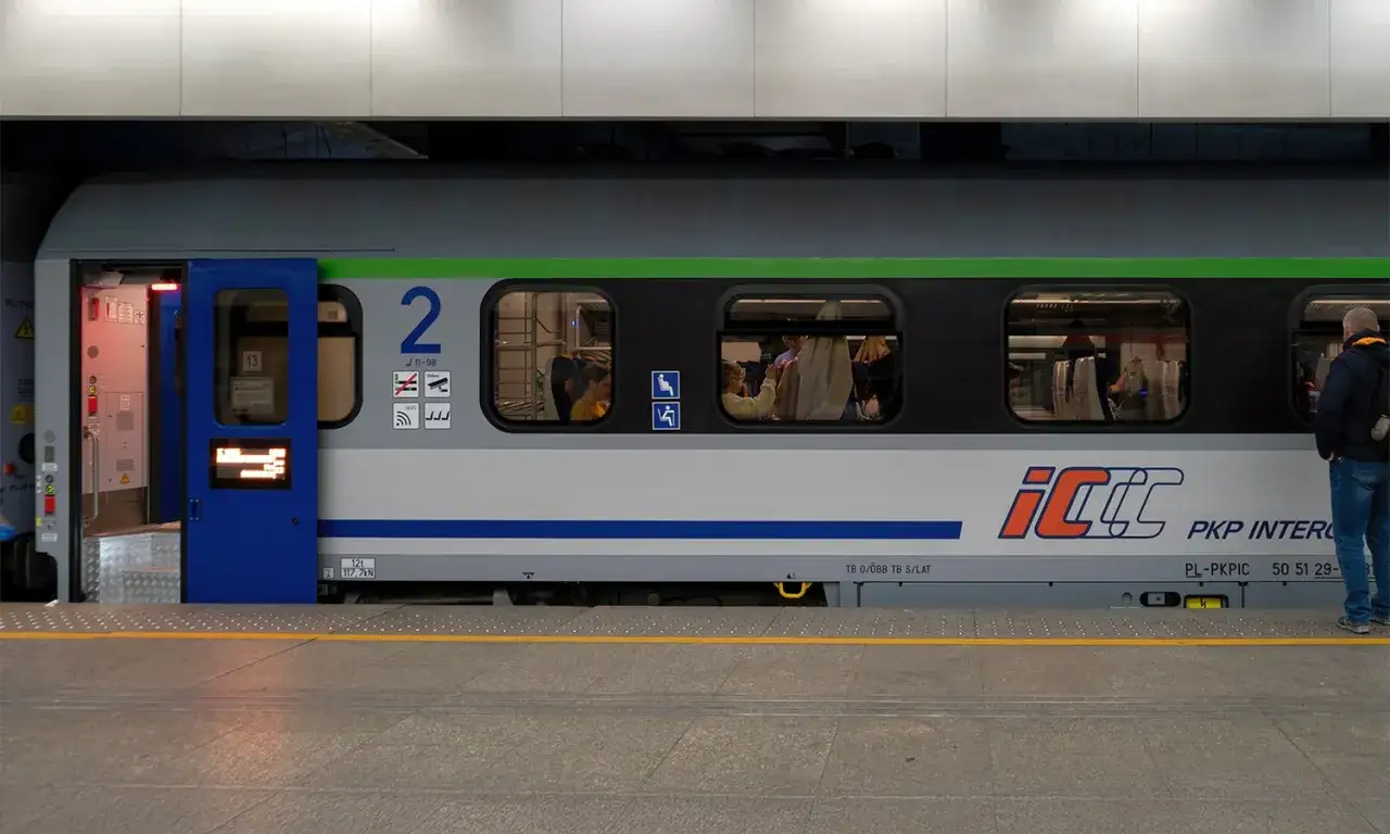 Pociąg PKP Intercity z dostępnym intercity wifi. Widać pasażerów w środku i mężczyznę stojącego na peronie.
