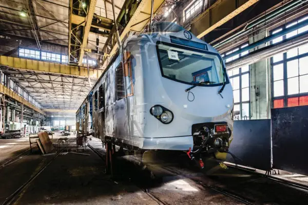 Nowy pociąg EN57 przechodzi modernizację w hali produkcyjnej. Widać jego front i część wagonu.